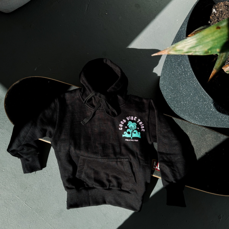 Kid wearing black “Good Vibe Tribe” hoodie with neon green and pink print. Eco-friendly surf hoodie for bold little legends. Durable, comfy, and made for chaos.