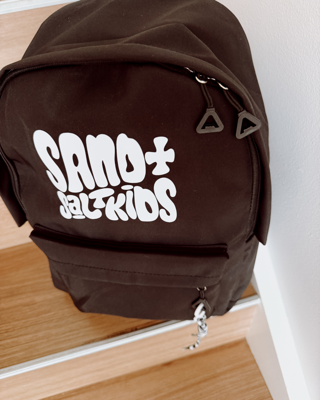 Black kids backpack with Sand + Salt Kids logo, multiple pockets and rope keychain detail.