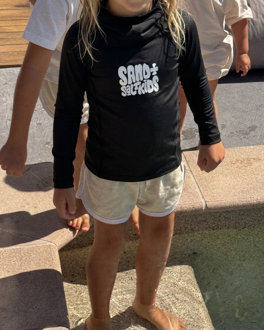kids wearing black Sand + Salt Kids long sleeve rash vest standing at pool edge