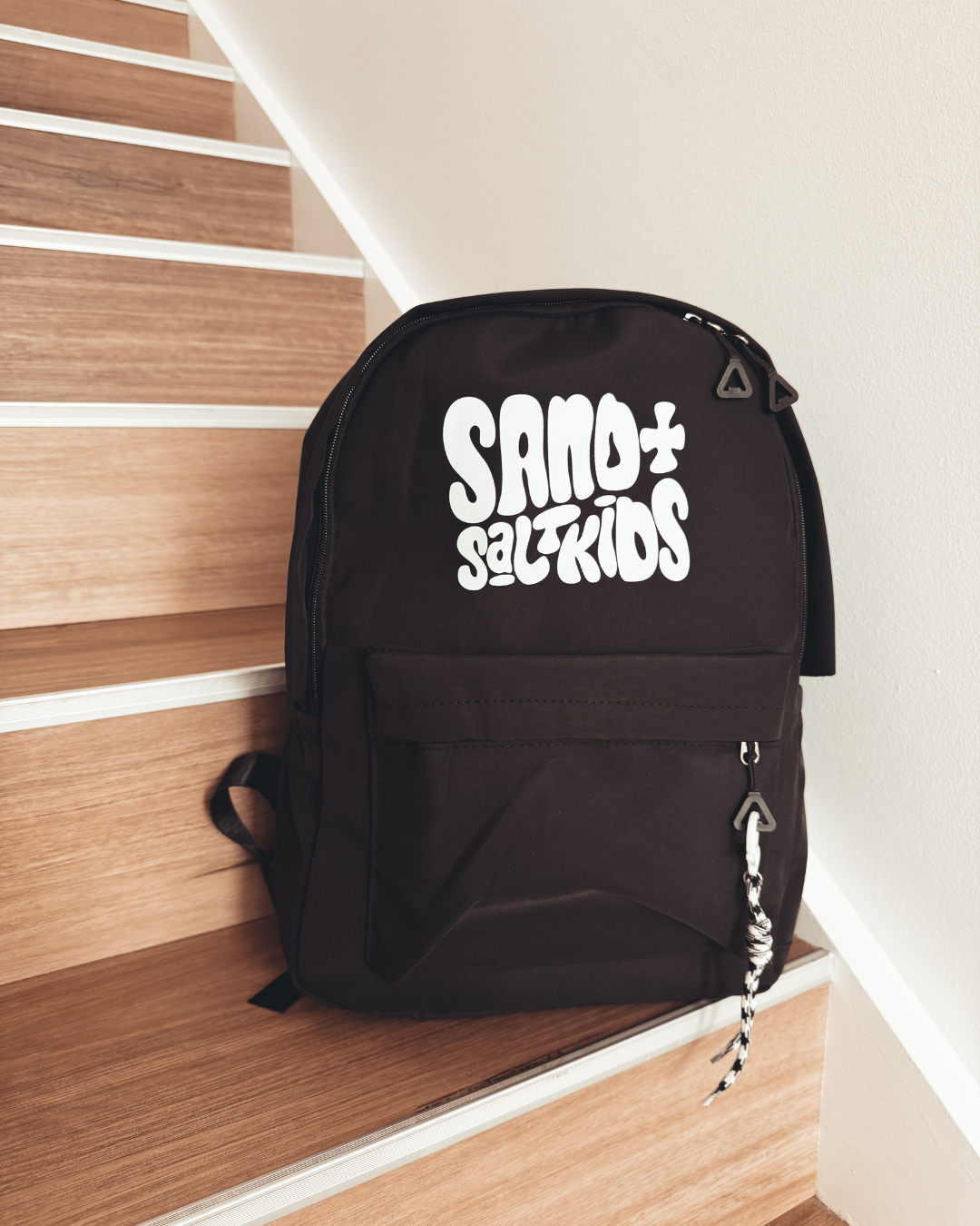 Black kids backpack with Sand + Salt Kids logo, multiple pockets and rope keychain detail.
