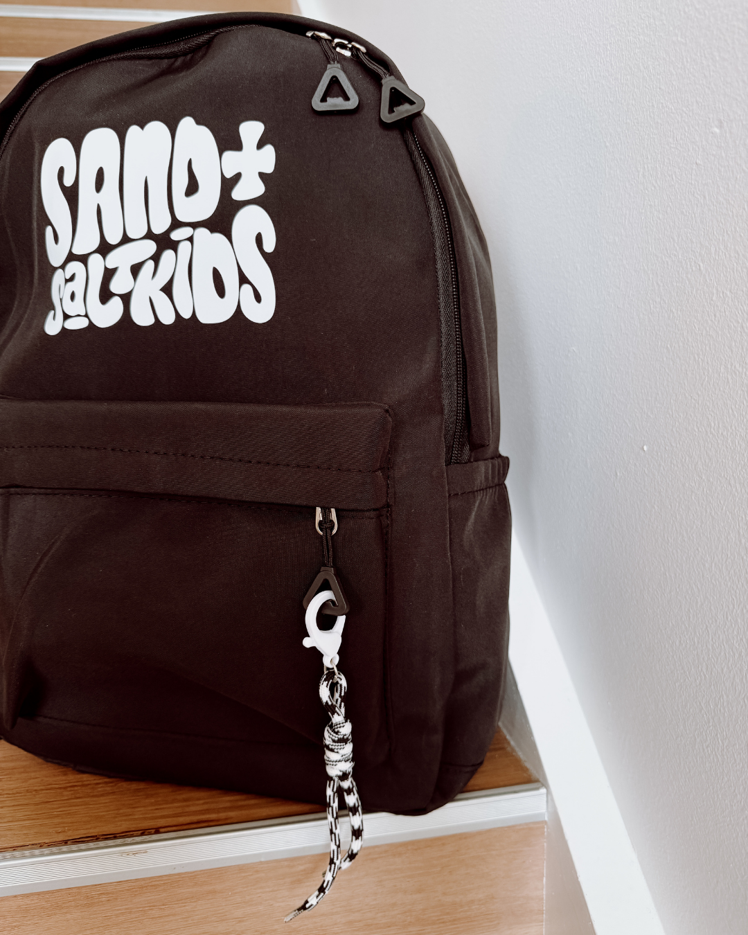 Black kids backpack with Sand + Salt Kids logo, multiple pockets and rope keychain detail.