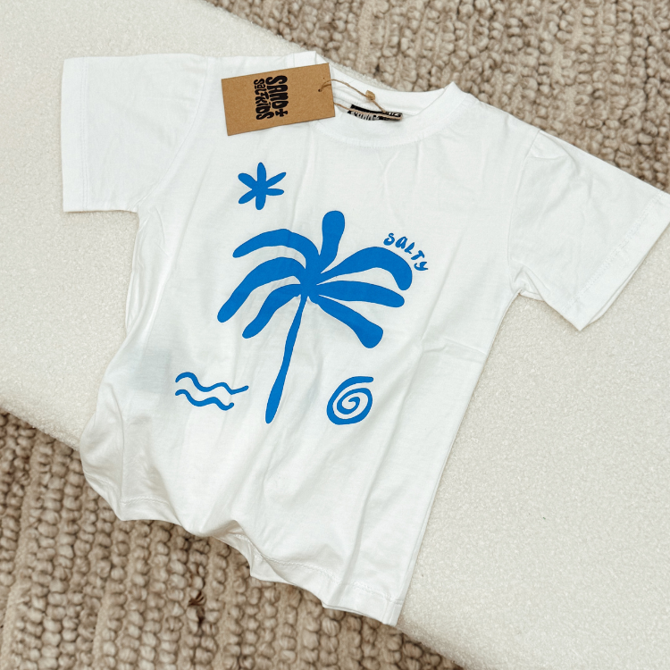 Flatlay of white Salty kids tee with bold chest print. Handmade kids surf t-shirt for summer beachwear.