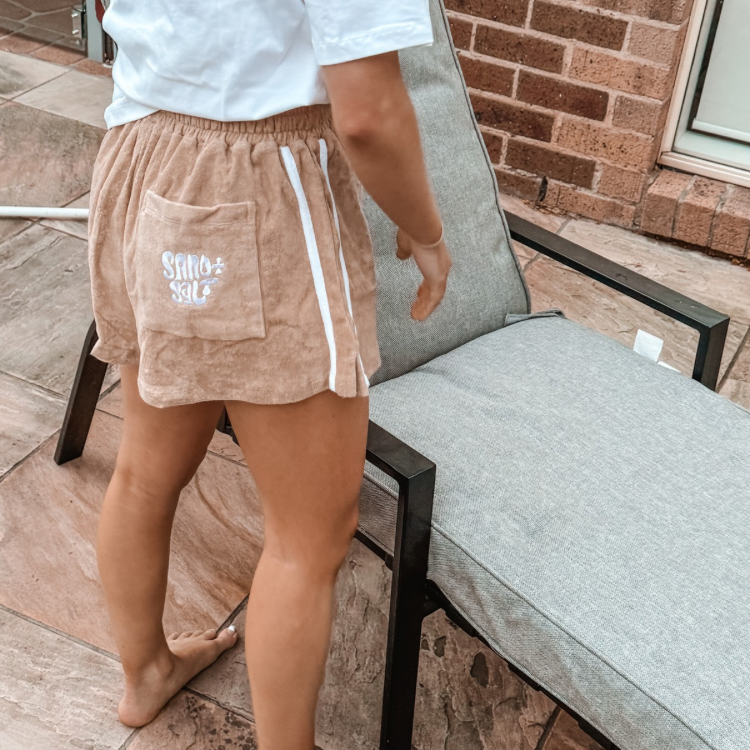 Woman wearing terry towelling shorts, walking barefoot at the beach. Ethical slow fashion for women.