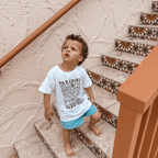 Child wearing white Paradise tee at the pool, surf-inspired design