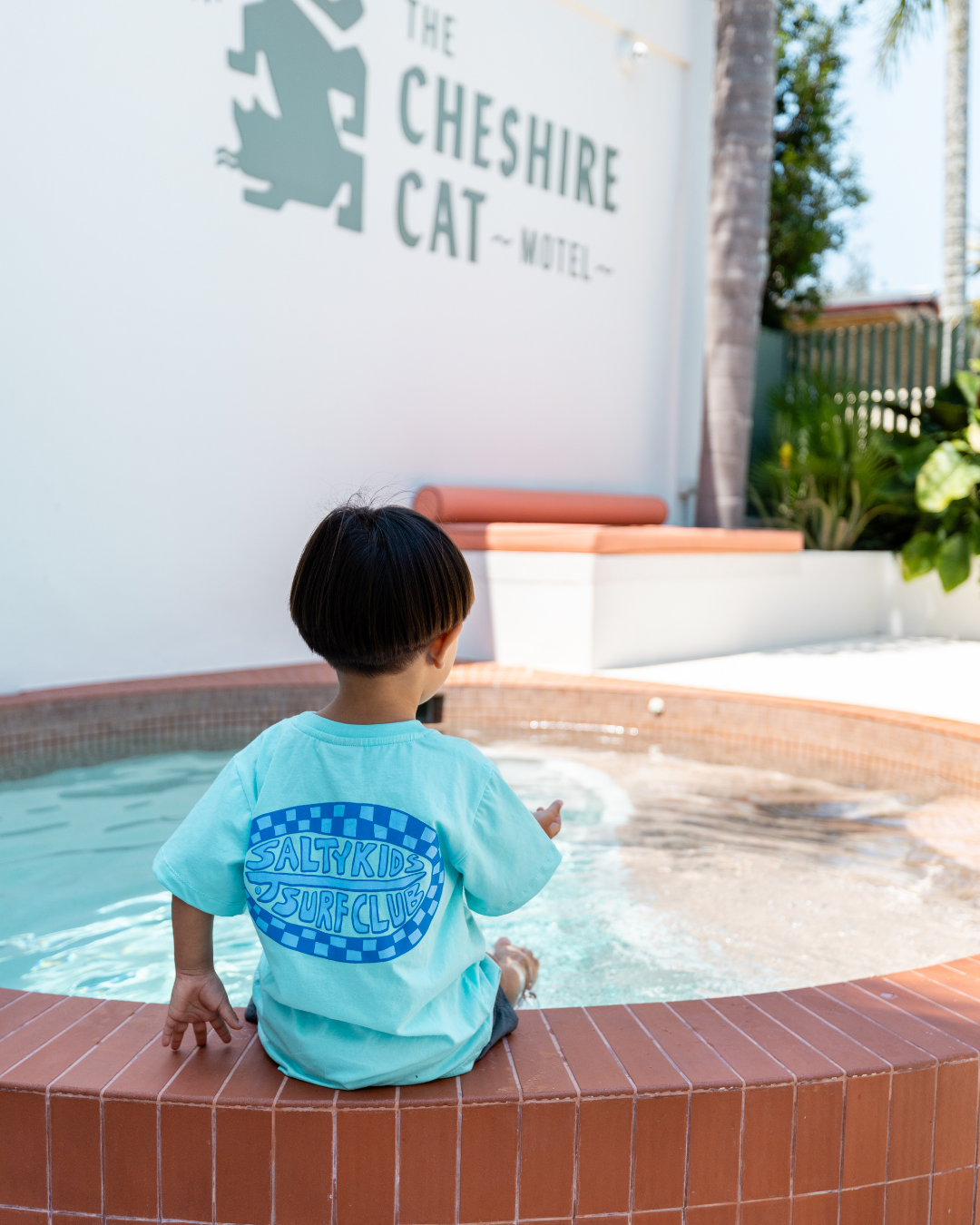 Child wearing Sand and Salt Kids Salty Kids Surf Club t-shirt by the pool, soft cotton kids tee designed for everyday play and summer adventures